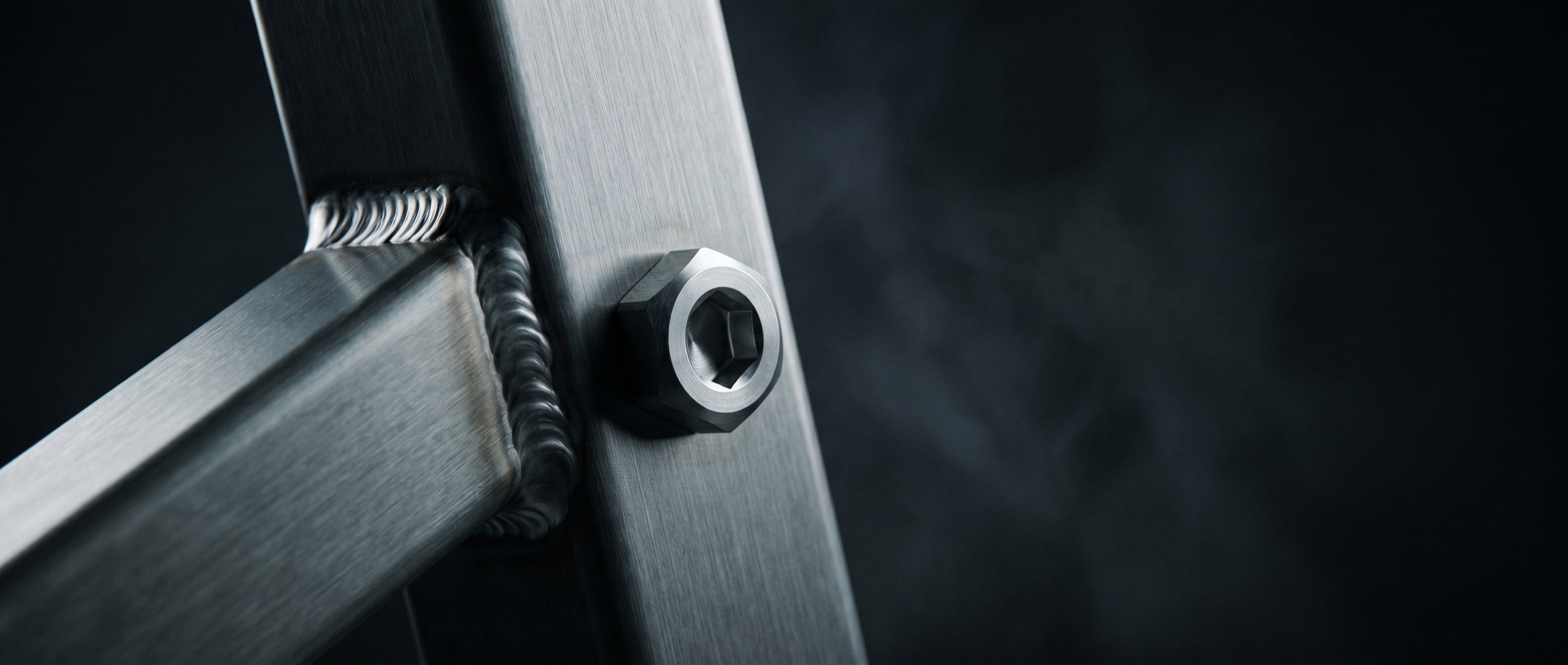 Brushed steel frame joint with a precision weld seam and machined bolt